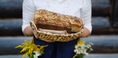 Baker's hands holding loaves of homemade bread in a wooden basket against the background of grass. Yeast-free wheat and rye bread with sourdough. Family bakery. The concept of eco food and productsの写真素材