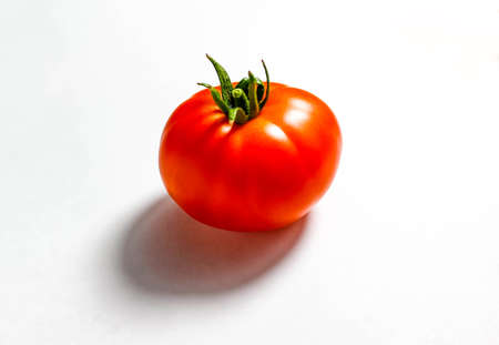 A ripe red tomato on a white background with a clear shadow. Top view, selective shot.