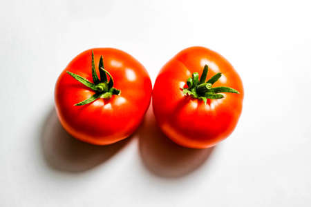 Two red tomatoes on a white background with clear shadows. The view from the top.