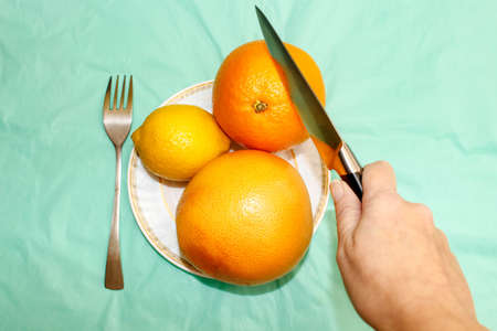 Hands that hold a fork and a knife for cutting an orange on a plate. HLS. Top view, selective shot.の写真素材