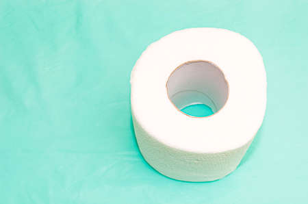 A roll of white toilet paper on a turquoise background. Close-up, selective shot.の写真素材