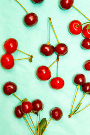 Cherry berries on a turquoise background, top view. The pattern is made from fresh berries. The...