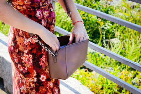 A woman is looking for something in her purse on the street. Photo of the lower body. Close up.