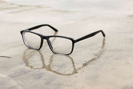 Glasses with diopters lie on the wet sand on the beach. Close-up, selective focus.