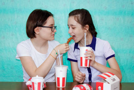 Chelyabinsk, Russia-June 16, 2020: Two Schoolgirls' sisters chat at the table, eat burgers and drink...