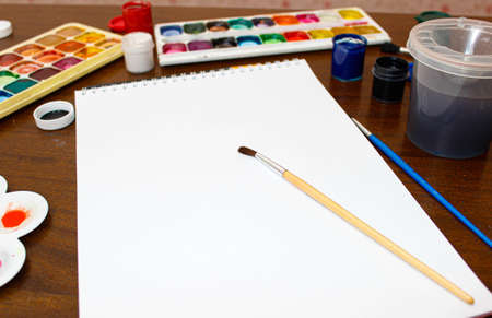 Watercolors, brushes and drawing paper are prepared on the table. Selective focus.
