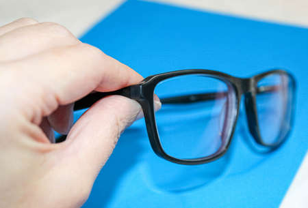 Hand holding glasses with diopters in black frames. Close-up, selective focus.