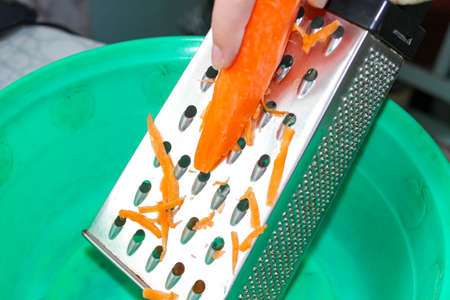 A woman's hand rubs carrots on a metal grater. Close up.の写真素材