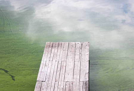Old wooden pier on the lake. Development of phytoplankton that causes changes in the color of water. The view from the top.の写真素材