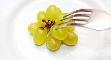 Green grapes on a plate, which is impaled on a fork. The concept of healthy and proper nutrition. Close-up, selective shot.の写真素材