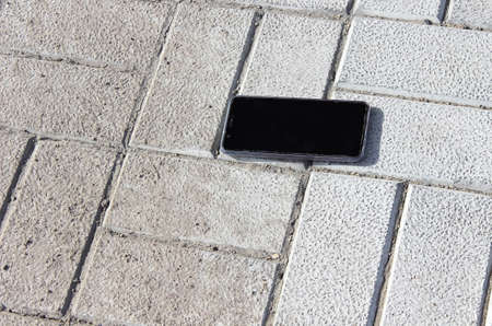 The lost smartphone is lying on the sidewalk. Carelessness.