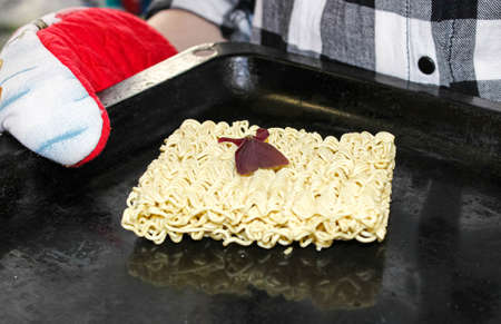 A hungry person about to cook instant noodles on a baking sheet in the oven. Joke.