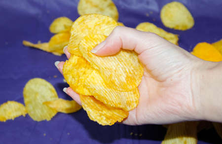 A woman's hand lifted an armful of potato chips from the dark blue tablecloth. Close up.