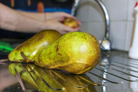 Two green pears are washed near the sink in the kitchen. Close-up, selective shot.