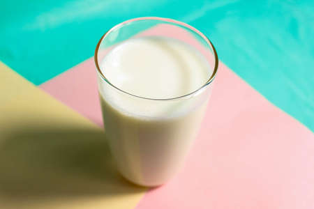 A glass of milk with a shadow on a colored background. Close-up, selective shot.の写真素材
