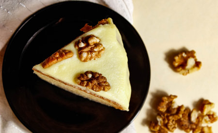 Sponge cake with walnuts and light cream on a black saucer. Top view, selective shot.