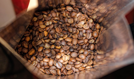 Roasted coffee beans that are filled in a craft bag are shiny inside. Top view, selective shot.