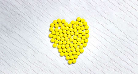 Yellow tablets are laid out on a light surface in the shape of a heart. The view from the top.