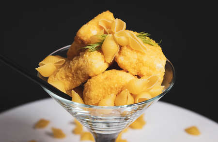 A glass cocktail glass containing nuggets and pasta, with a drinking straw. Creative still life....