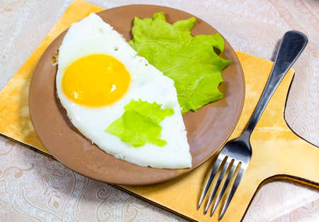 Fried eggs on a plate on the table with a green lettuce leaf. Close-up, selective shot.