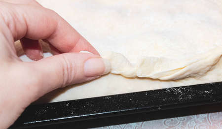 A woman's hand pinches the dough on a baking sheet. Cooking a homemade cake. Close-up, selective shot.の写真素材