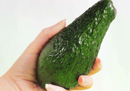 A woman's hand holds a whole green avocado. Close-up, selective shot.