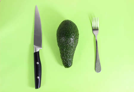 A whole avocado is on the table and a fork and knife are next to it. The concept of dietary proper nutrition. Top view, selective shot.の写真素材