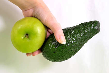 A woman's hand holding a green avocado and an apple. The concept of weight loss and proper nutrition. Close-up.の写真素材