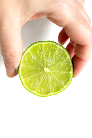A woman's hand holds half a lime with her fingers on a light background. The concept of healthy eating. Vertical frame.の写真素材