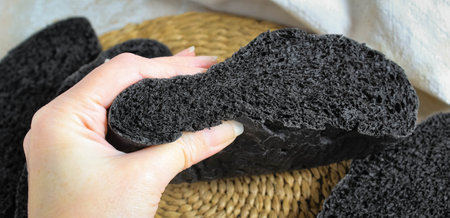 A womans hand clutching a sliced loaf of black bread with activated carbon.の写真素材