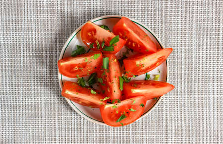Sliced red tomato slices on a plate, sprinkled with spices and green onions. Top view.の写真素材