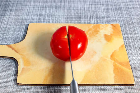 A red tomato on a chopping board is cut with a knife. Close-up.の写真素材