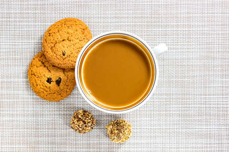 Coffee and milk in a mug, oatmeal cookies and candy on the table next to it. Top view.の写真素材
