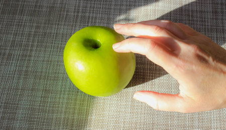 A woman's hand that reaches for a green apple. Natural sunlight with sharp shadows. Close-up.の写真素材