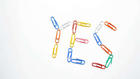 The word Yes is laid out of colored paper clips on a light background. Top view.