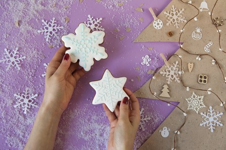 Female hands holding two little snowflakes gingerbread on table with Christmas decorations. Cut paper in fir-tree shape. View from aboveの写真素材