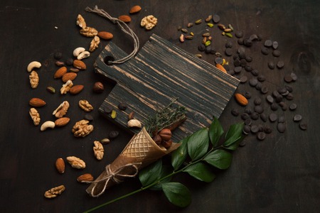 Assorted mixed nuts and chocolate on a wooden cutting board. Close up, cone with nuts and branch of the leaves, selective focus. The concept of proper nutrition.の写真素材