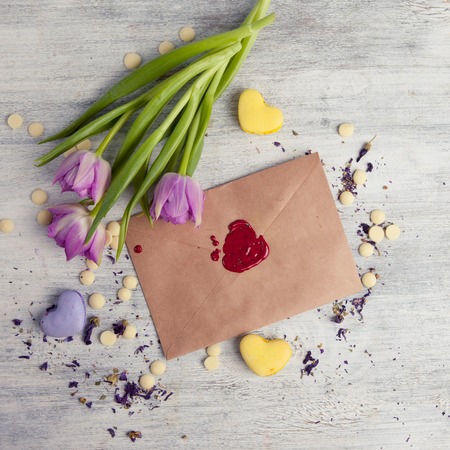 Envelope with wax seal on wooden background. Flowers tulips and heart shaped macaroons cookies. Concept the Feast Day of Holiday Valentine's Day. Top viewの写真素材