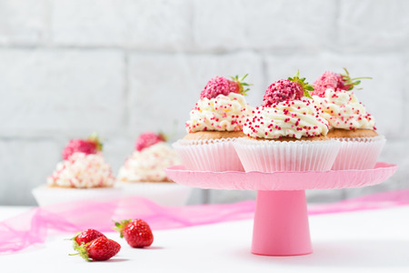 Vanilla cupcakes decorated strawberries on a pink cake standの写真素材