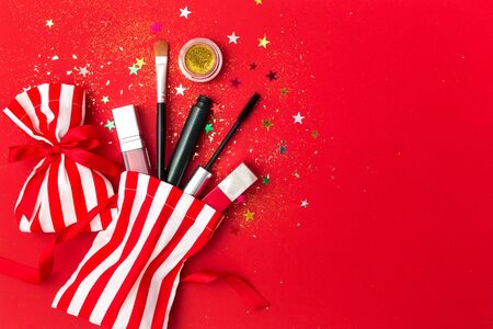 Christmas background with mascara, lipstick and shadows. Flat lay composition with sparkles, gift bags and cosmetic products for the New Year party.の写真素材