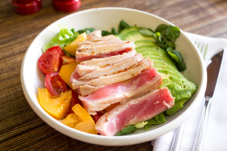 Bowl with tuna, avocado and tomatoes on a wooden tableの写真素材