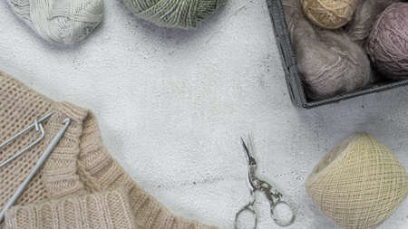 a knitted sweater, knitting needles and multi-colored yarn for knitting lie on a light concrete...