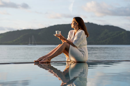 brunette white bathrobe sits at edge of pool overlooking Indian Oceanの写真素材