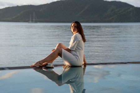 brunette white bathrobe sits at edge of pool overlooking Indian Oceanの写真素材