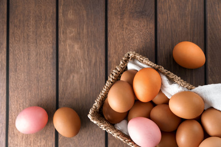 A mixture of brown and pink eggs displayed in a basket on a wooden table, creating a rustic and...