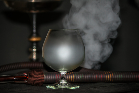 Heavy hookah smoke under a brandy glass on a gray background, hookah tube