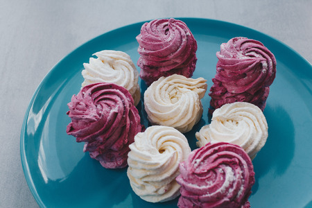 White mango and pink blueberry marshmallows or zephyr with sugar powder on a blue plate. Homemade sweet.の写真素材