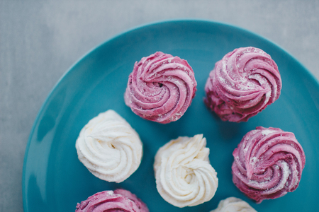 White mango and pink blueberry marshmallows or zephyr with sugar powder on a blue plate. Homemade sweet.の写真素材
