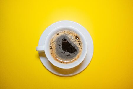 White coffee Cup with foam saucer on a bright yellow background top viewの写真素材
