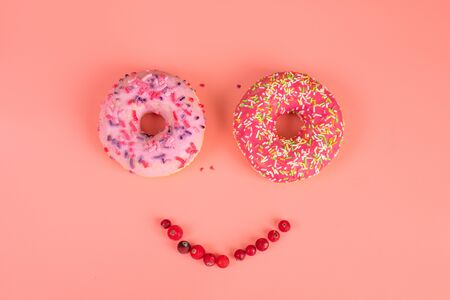 Round pink donuts on pink background with red cranberry berries. Copy space text. Glazed sprinkled donut.の写真素材